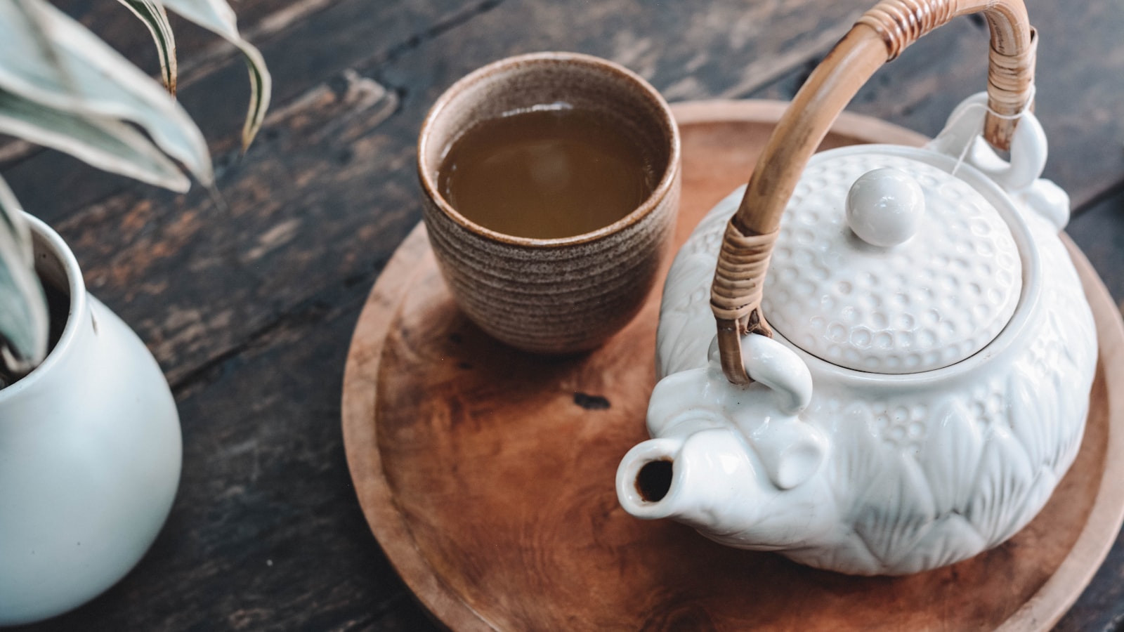 A cup of freshly brewed green tea beside loose green tea leaves